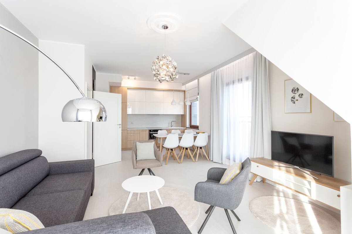 Un salon moderne comprenant un canapé, un fauteuil et un téléviseur, et donnant sur une cuisine et un coin repas.