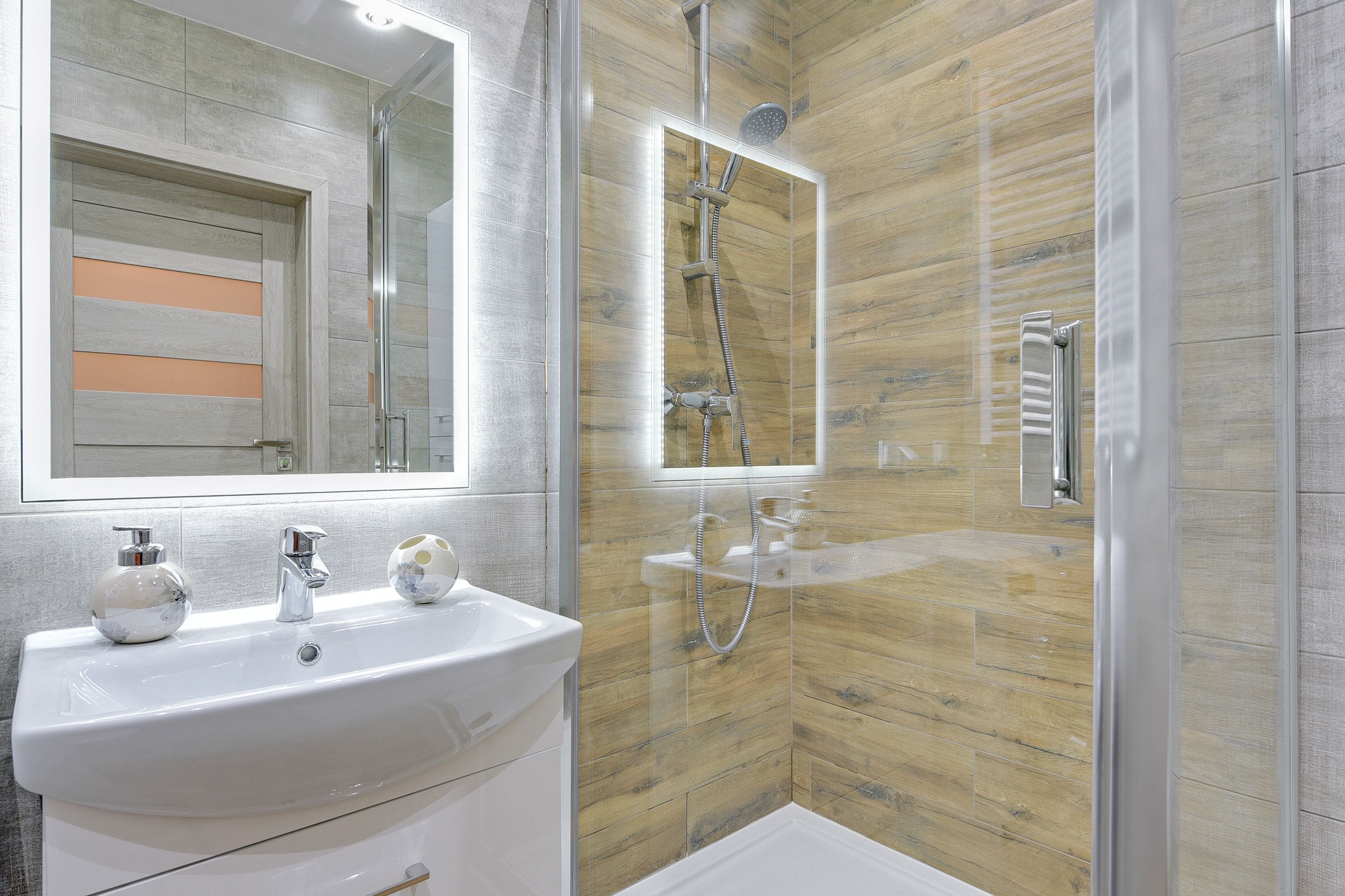 A modern bathroom with a glass-enclosed shower, a white sink with a mirror, and a wooden wall panel.