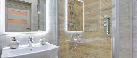 A modern bathroom with a glass-enclosed shower, a white sink with a mirror, and a wooden wall panel.