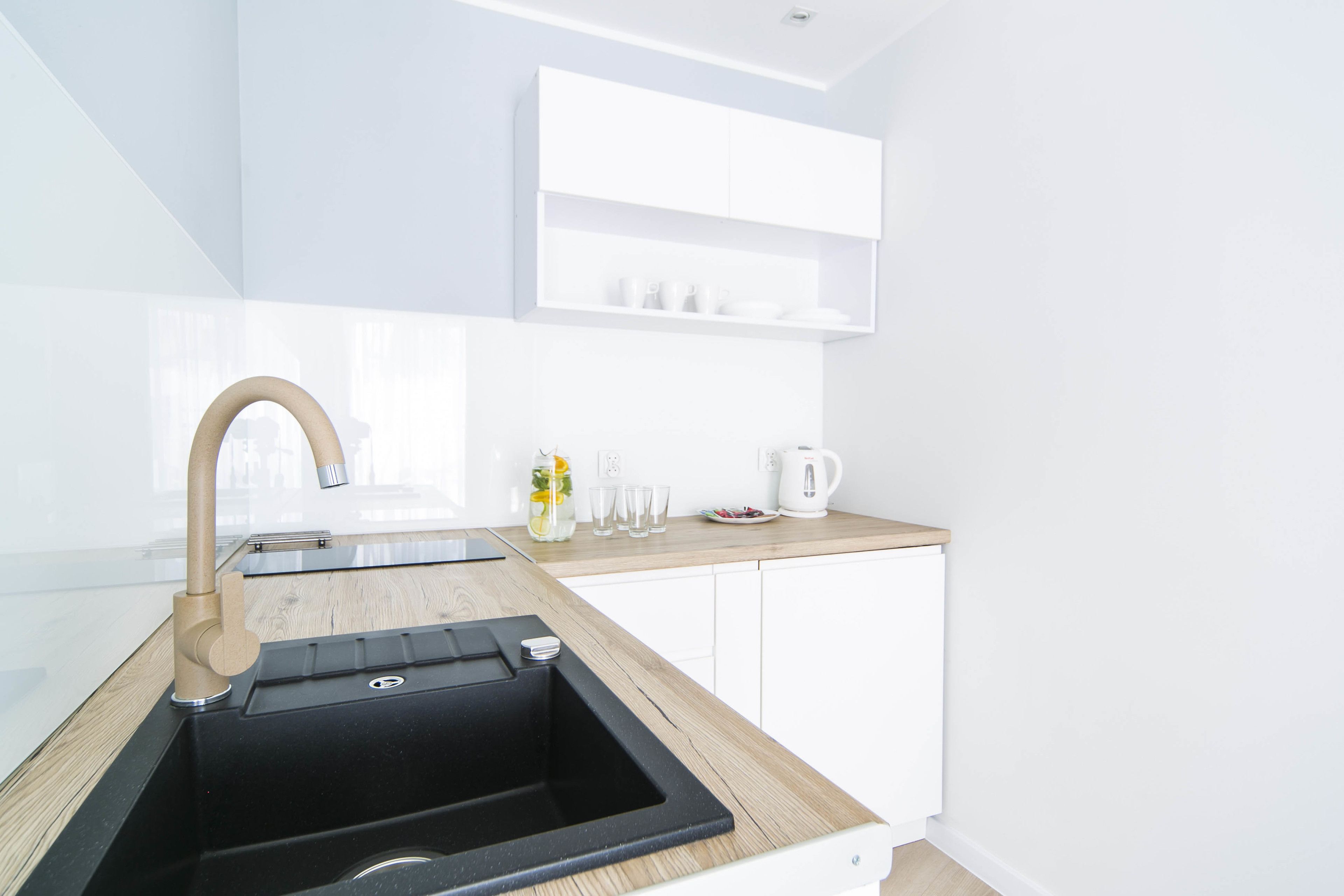 A modern kitchen with a black sink, wooden countertop, white cabinets, and a built-in shelf above the sink.