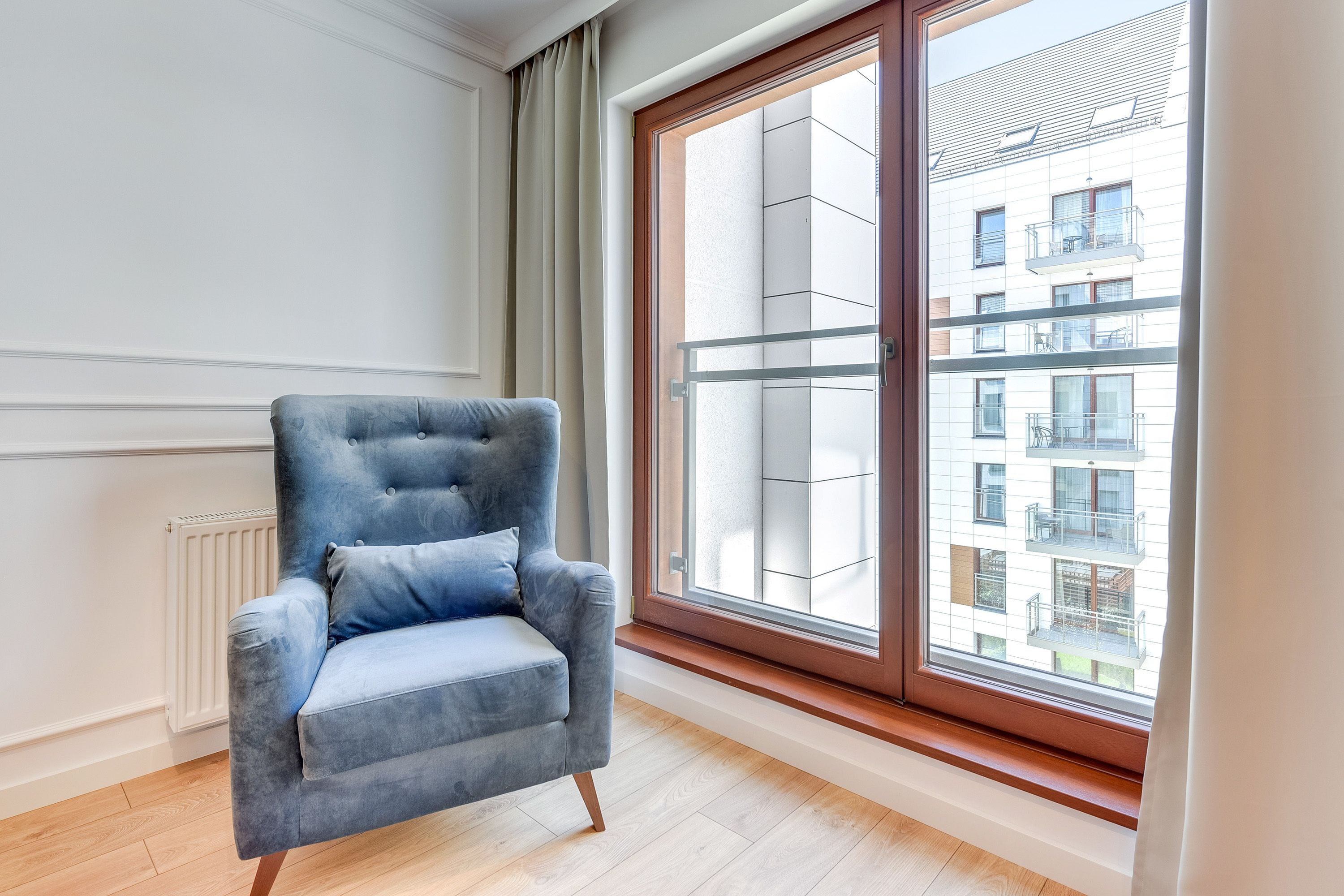 A room with a large window, a grey upholstered armchair, and a radiator.