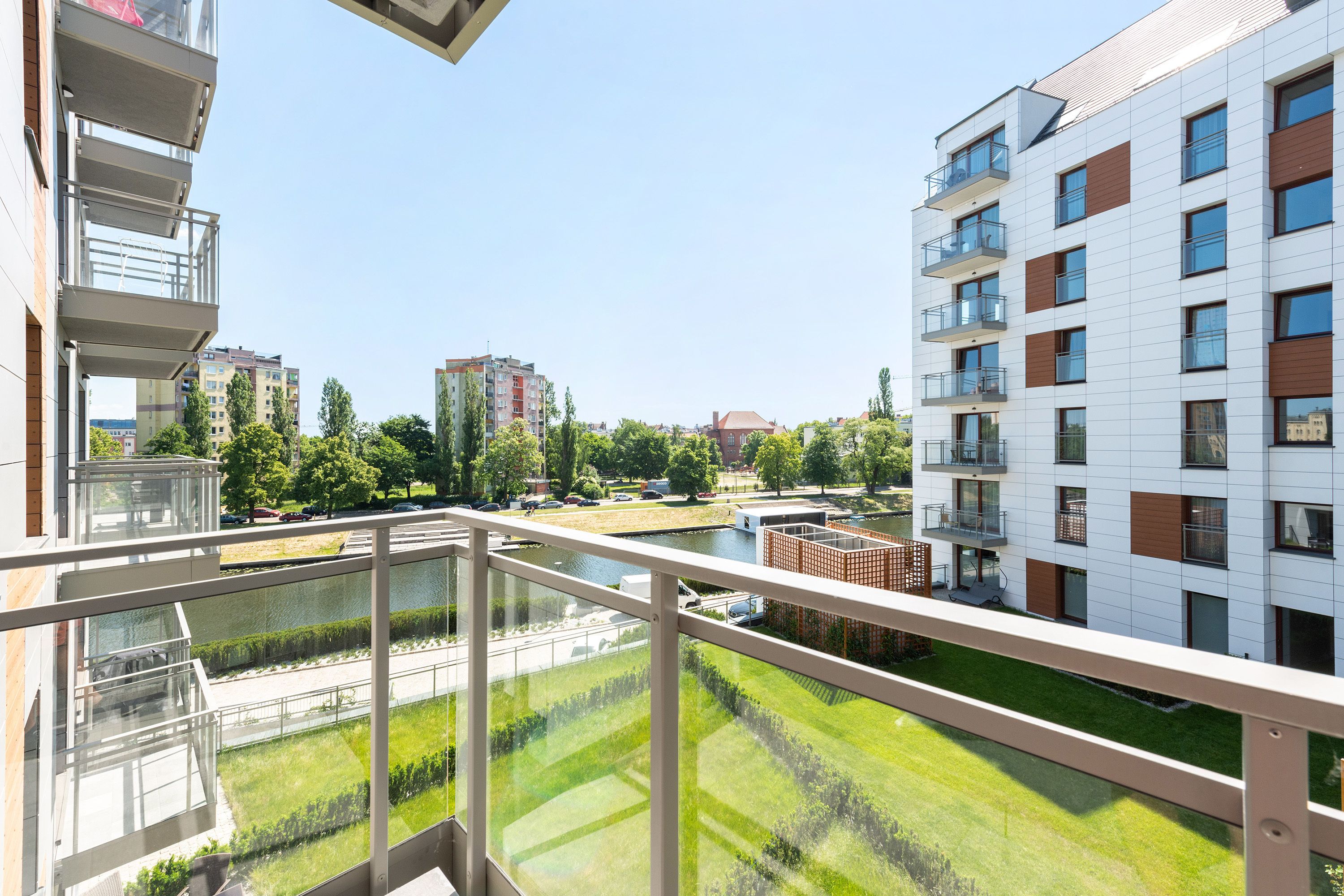 A modern apartment building with balconies, a river, and a park in the background.