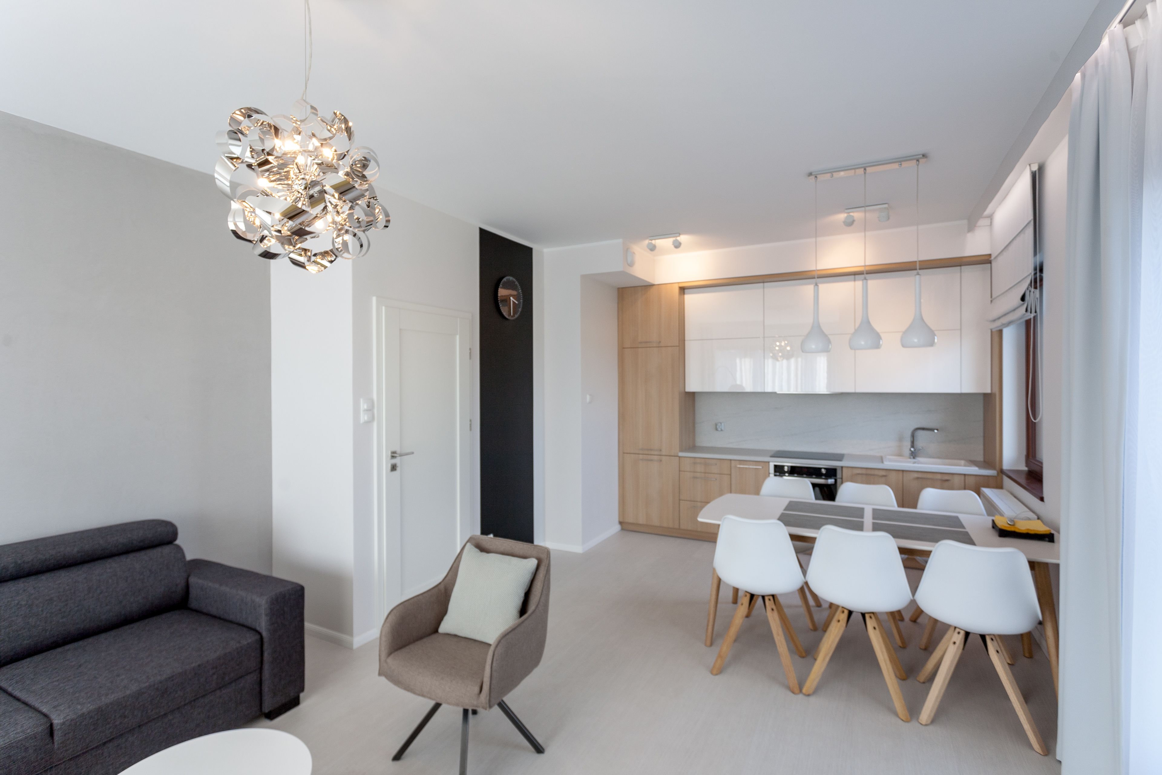 A modern kitchen with white cabinets, a dining table with four chairs, and pendant lights.