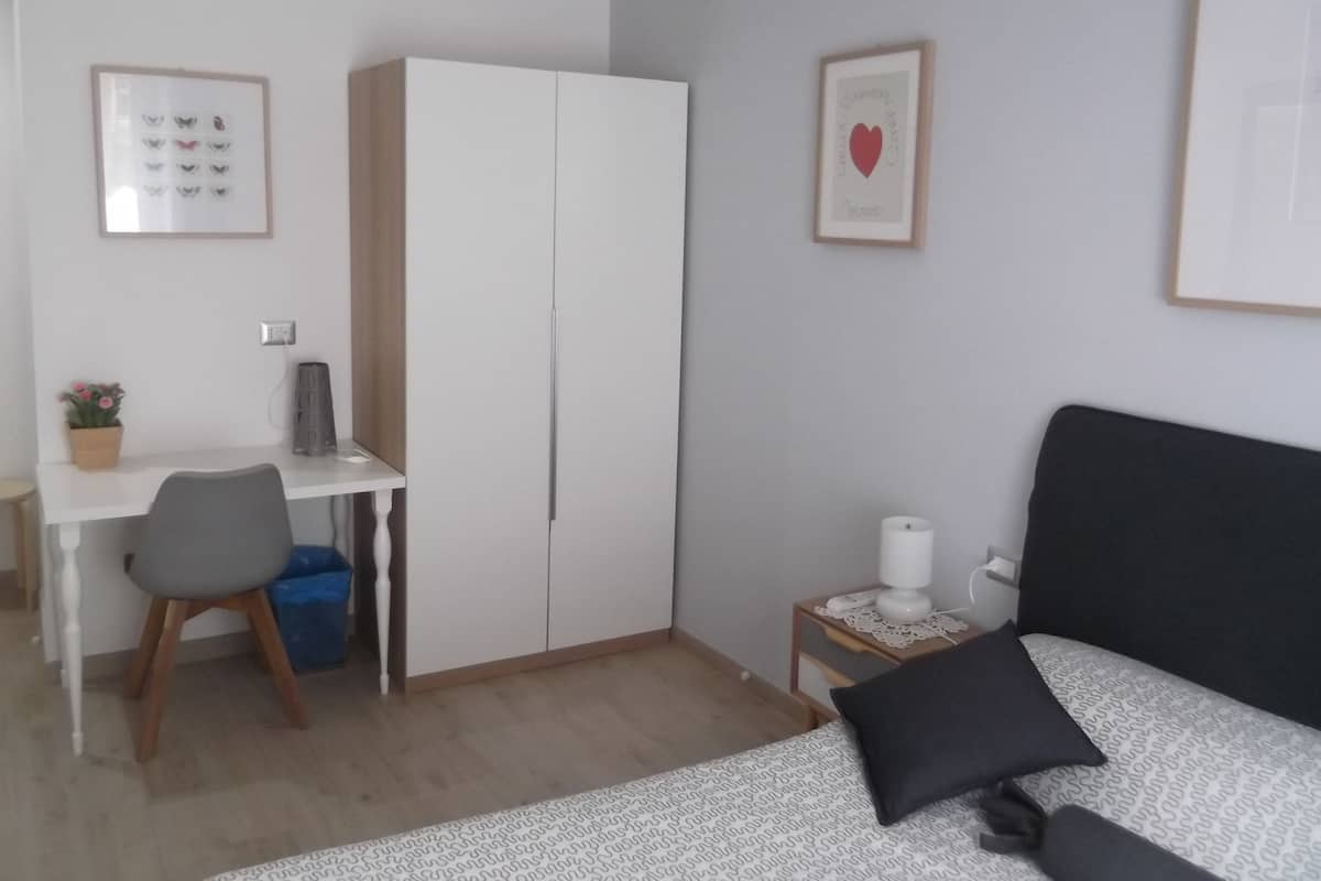 Een slaapkamer met een bed, bureau, kledingkast en nachtkastje.
