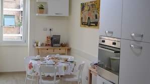 A kitchen with white cabinets, a dining table set with chairs, a ceiling fan, and a window with a view of a building.