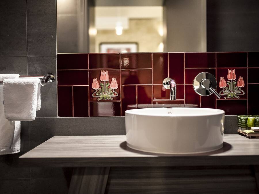 A bathroom with a round white sink, dark tiled walls, and a mirror.