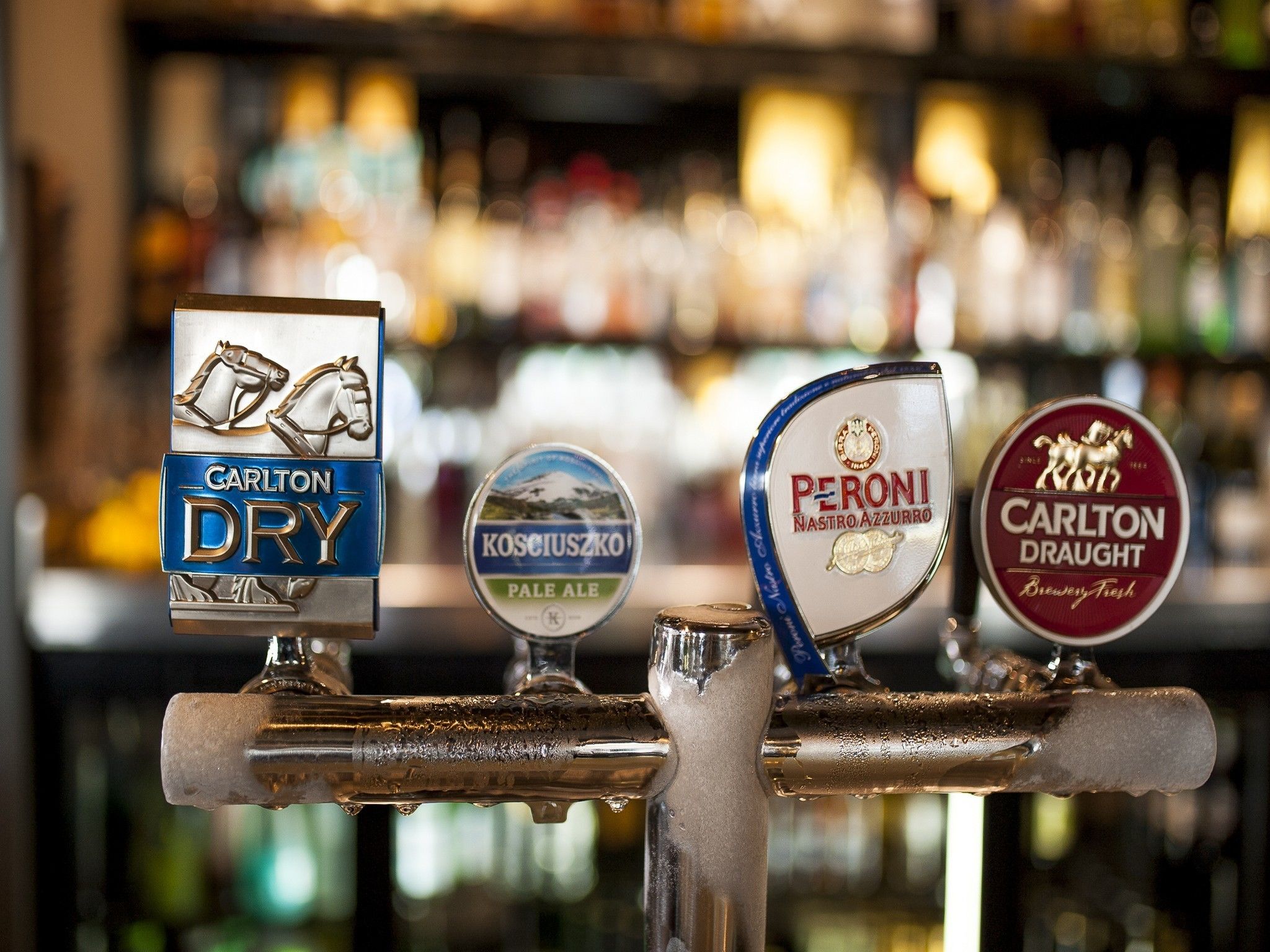 A bar tap with three beer taps labeled 'Carlton Dry', 'Kosciouszko Pale Ale', and 'Carlton Draught'.