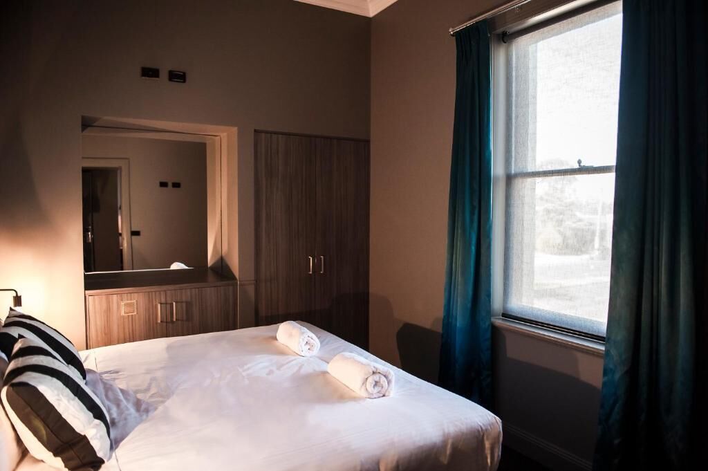 Una habitación de hotel con cama, un espejo grande, un armario y una ventana con cortinas.