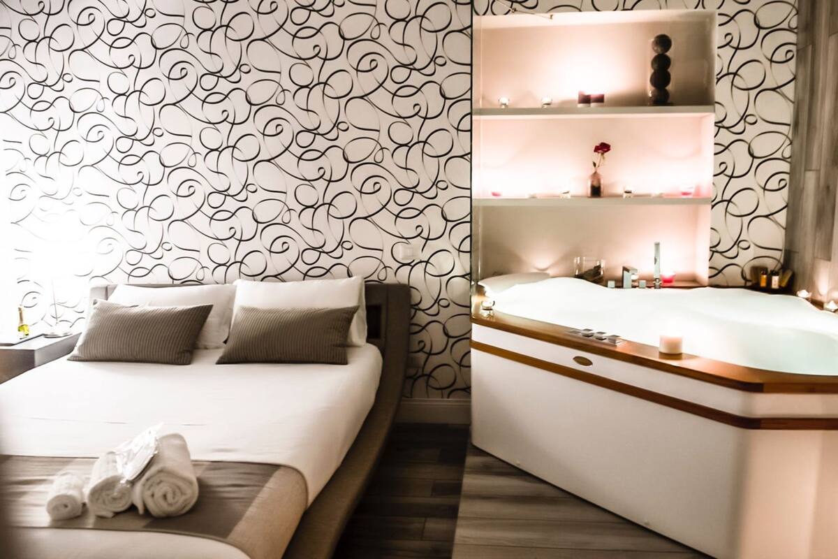 Una habitación de hotel con cama, baño con bañera y tocador con estantes.