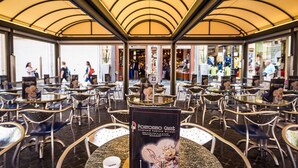 An indoor café with round tables and chairs, a central display with a sign, and a view of the street outside. - Domus Tacito Luxury (Rome)