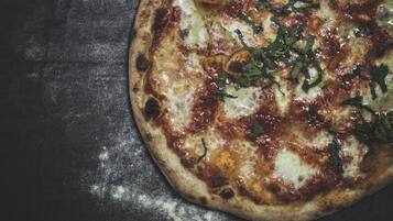 Una pizza con queso derretido y hierbas sobre una superficie oscura.
