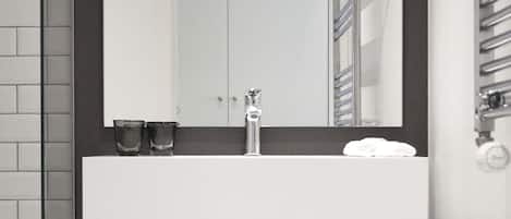 Un baño moderno con un lavamanos blanco, pared oscura y un espejo encima.