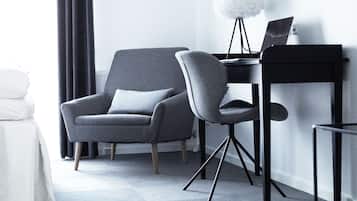 A modern room with a grey armchair, a small desk with a laptop, and a white lamp.