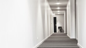 Un pasillo largo y estrecho con alfombra a rayas, paredes blancas y una puerta al final.