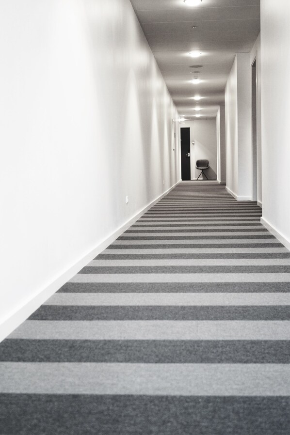 A long, narrow hallway with a striped carpet, white walls, and a door at the end.