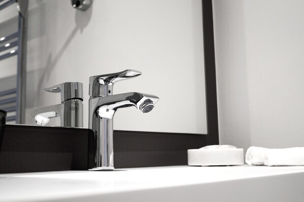 A modern bathroom with a chrome faucet, a mirror, and a white towel on the sink.