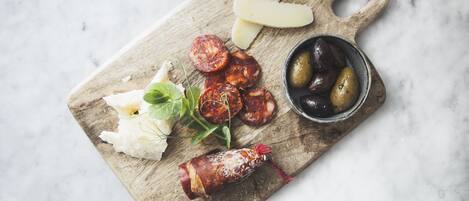 A wooden cutting board with sliced cured meats, cheese, olives, and greens.