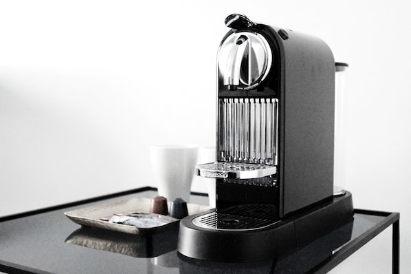 A compact espresso machine on a glass table with a tray of coffee capsules and a cup of coffee.