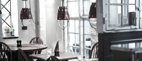 A dining area with wooden tables and chairs, hanging pendant lights, and a large window with a view of the outside.