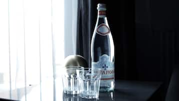 Una botella de agua y tres vasos sobre una mesa cerca de una ventana.