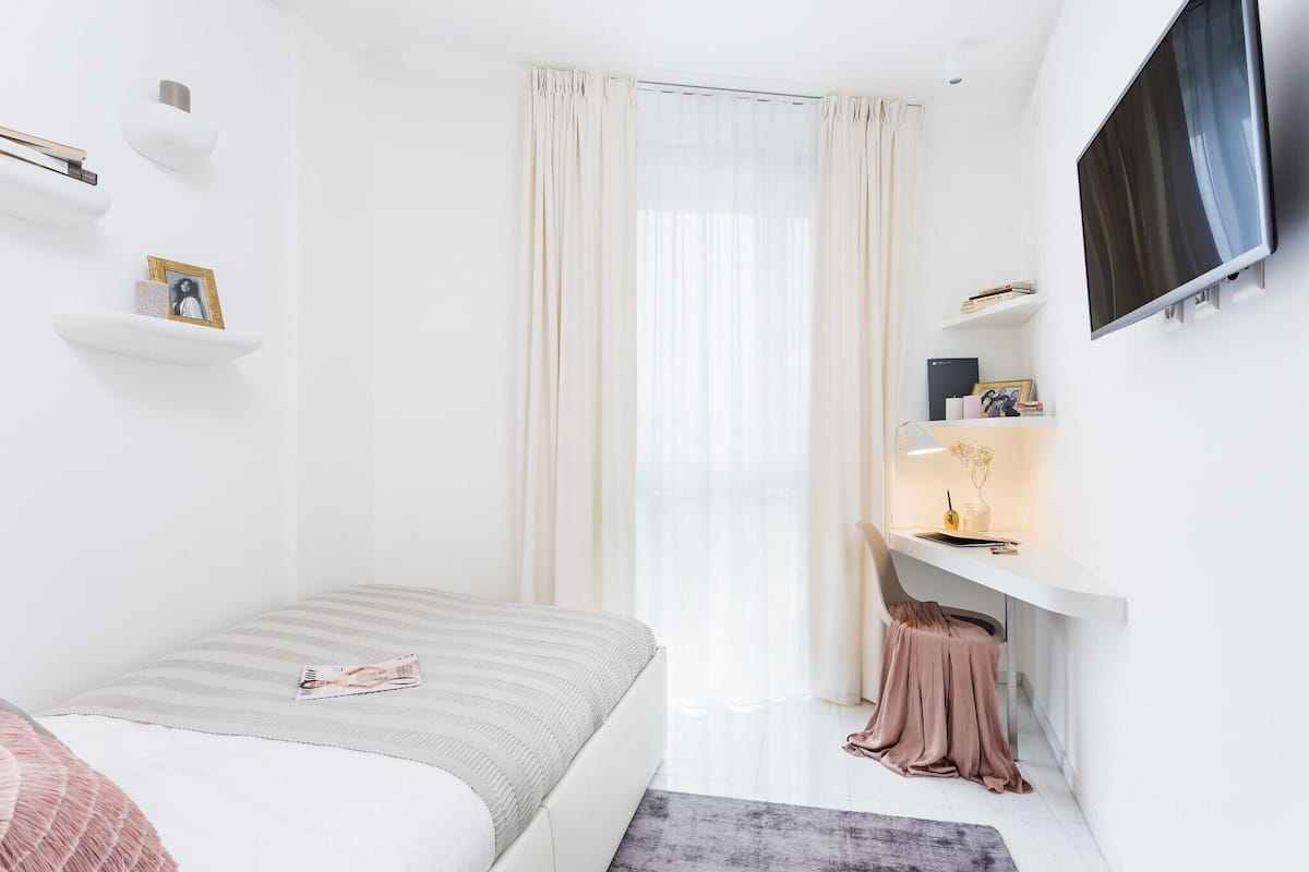 A modern bedroom with a bed, a desk, and a TV.