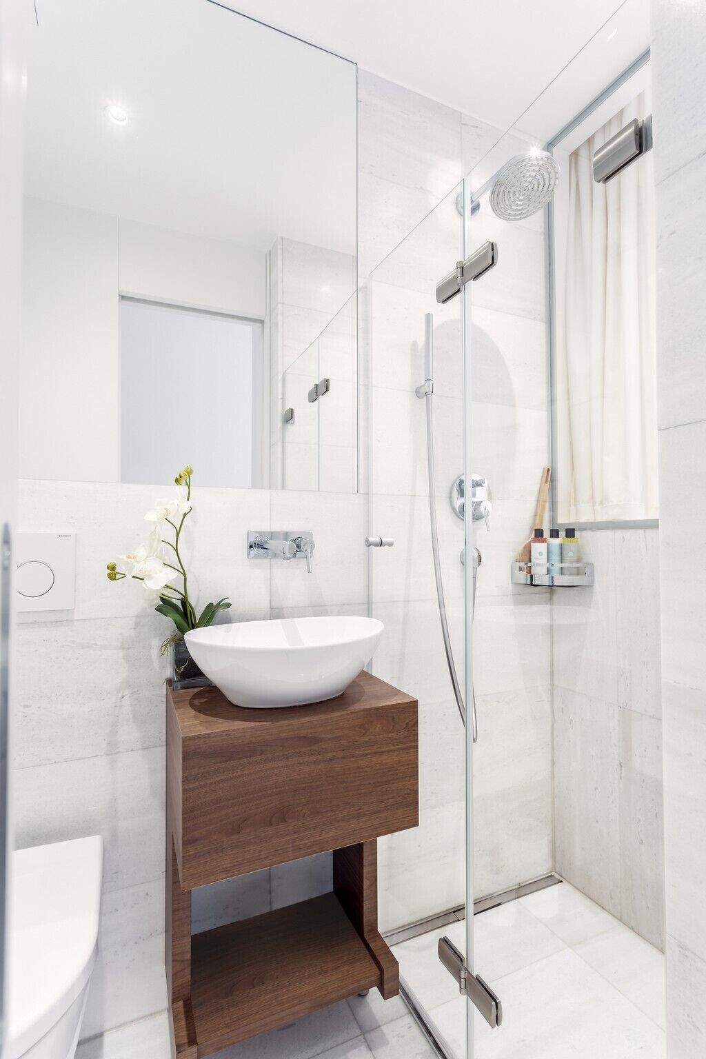 Une salle de bain moderne avec un lavabo sur pied blanc, un meuble-lavabo en bois, une cabine de douche en verre et un miroir.
