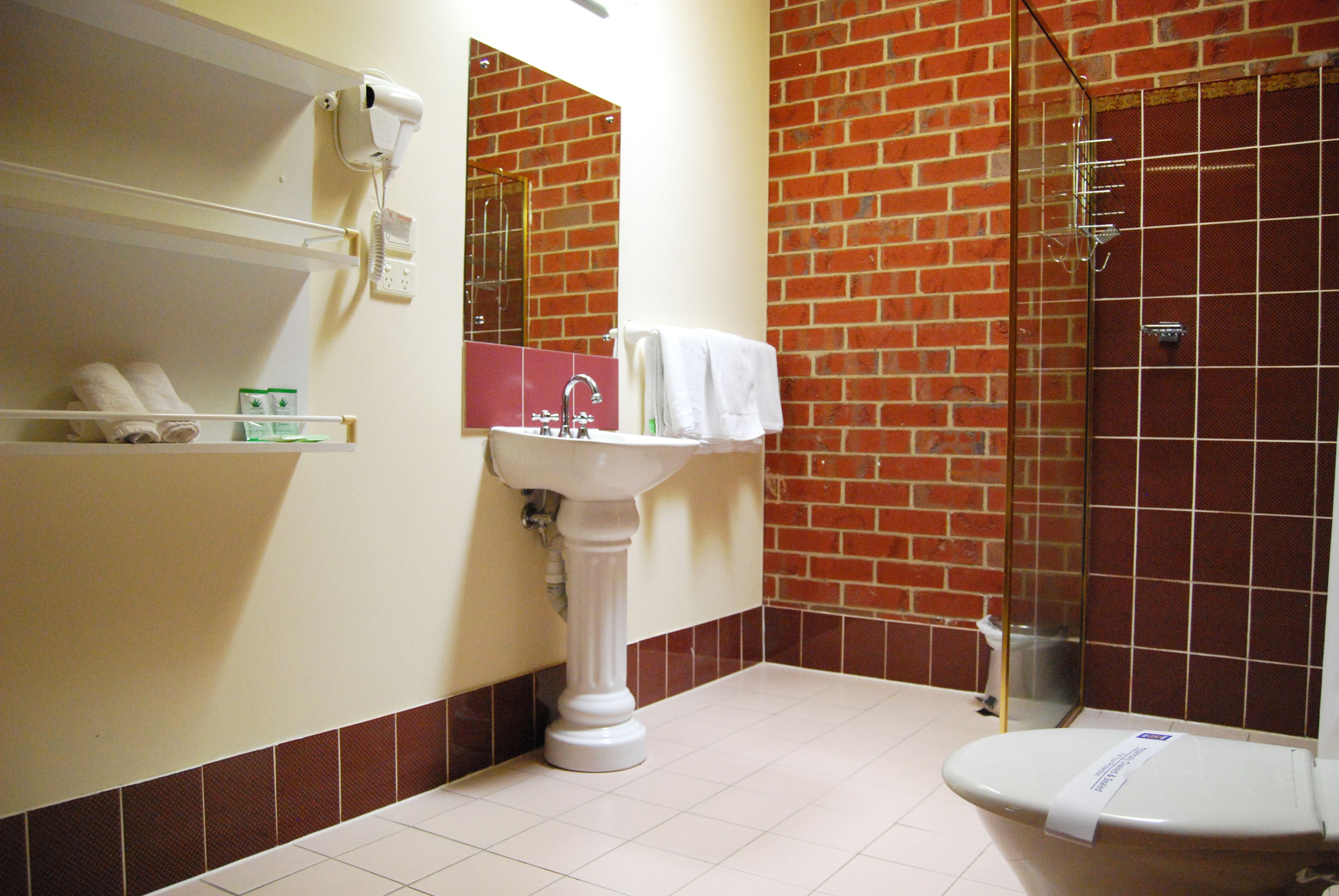 A bathroom with a white pedestal sink, a mirror, a white toilet, and a glass-enclosed shower.