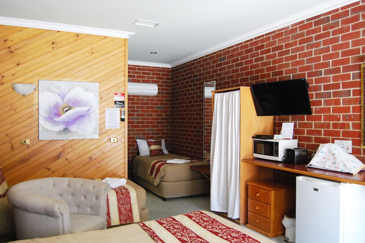 A compact room with a bed, a chair, a desk with a microwave, a TV, and a small refrigerator.