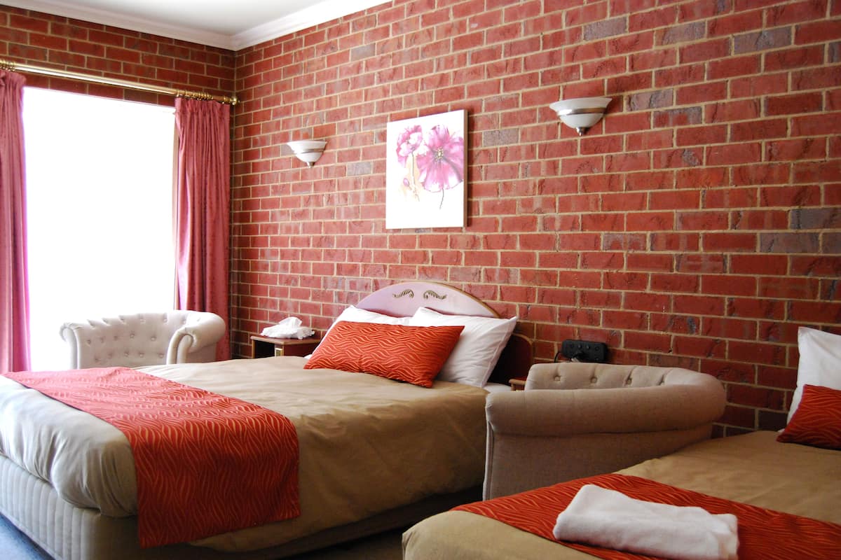 A hotel room with a brick wall, two beds, a chair, and a nightstand.