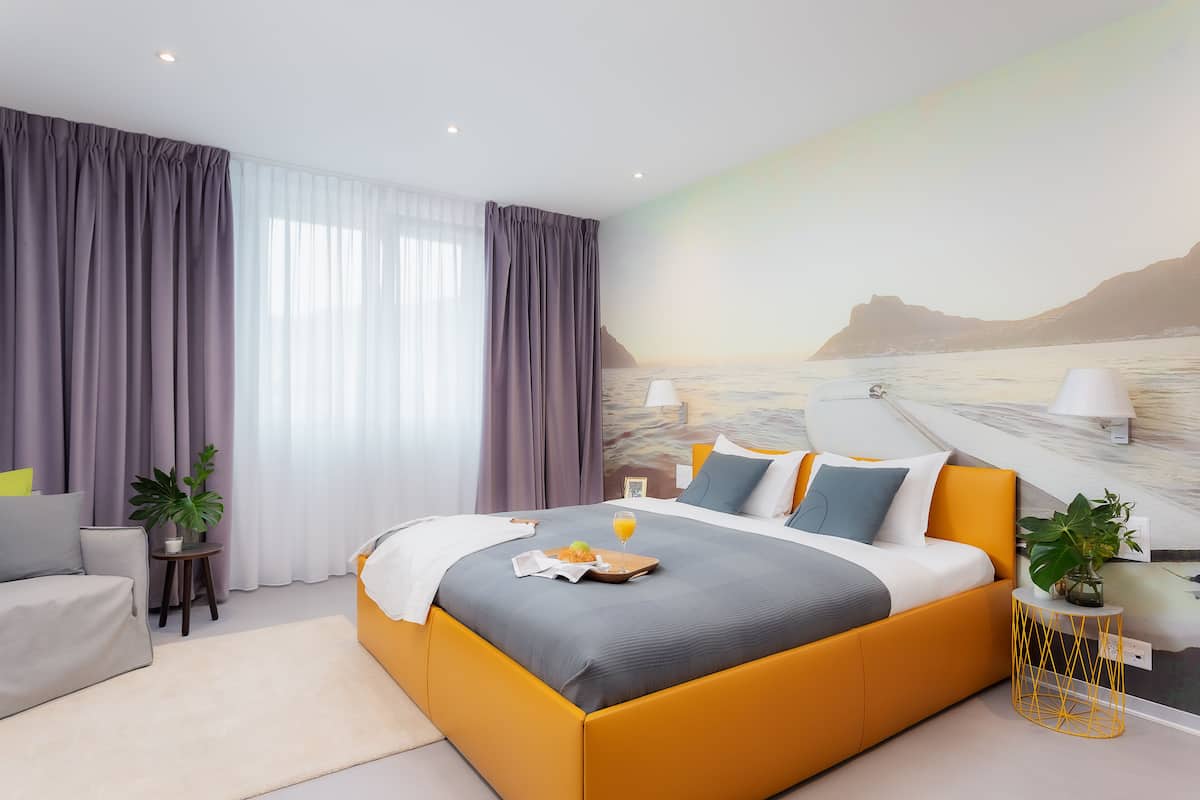 A modern bedroom with a large bed, a sofa, and a view of a beach through the window.