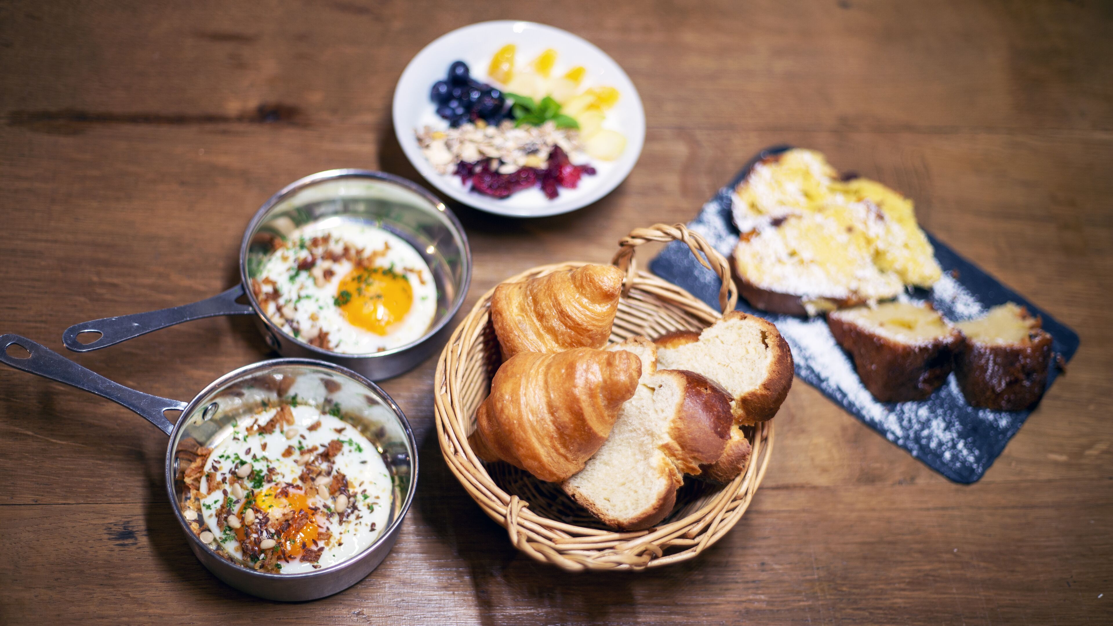 Una colazione con croissant, pane e una ciotola di frutta.