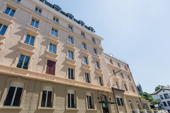 A multi-story building with a beige facade, multiple windows, and a visible entrance with a door and a sign. - VISIONAPARTMENTS Vevey Rue des Communaux (Vevey)