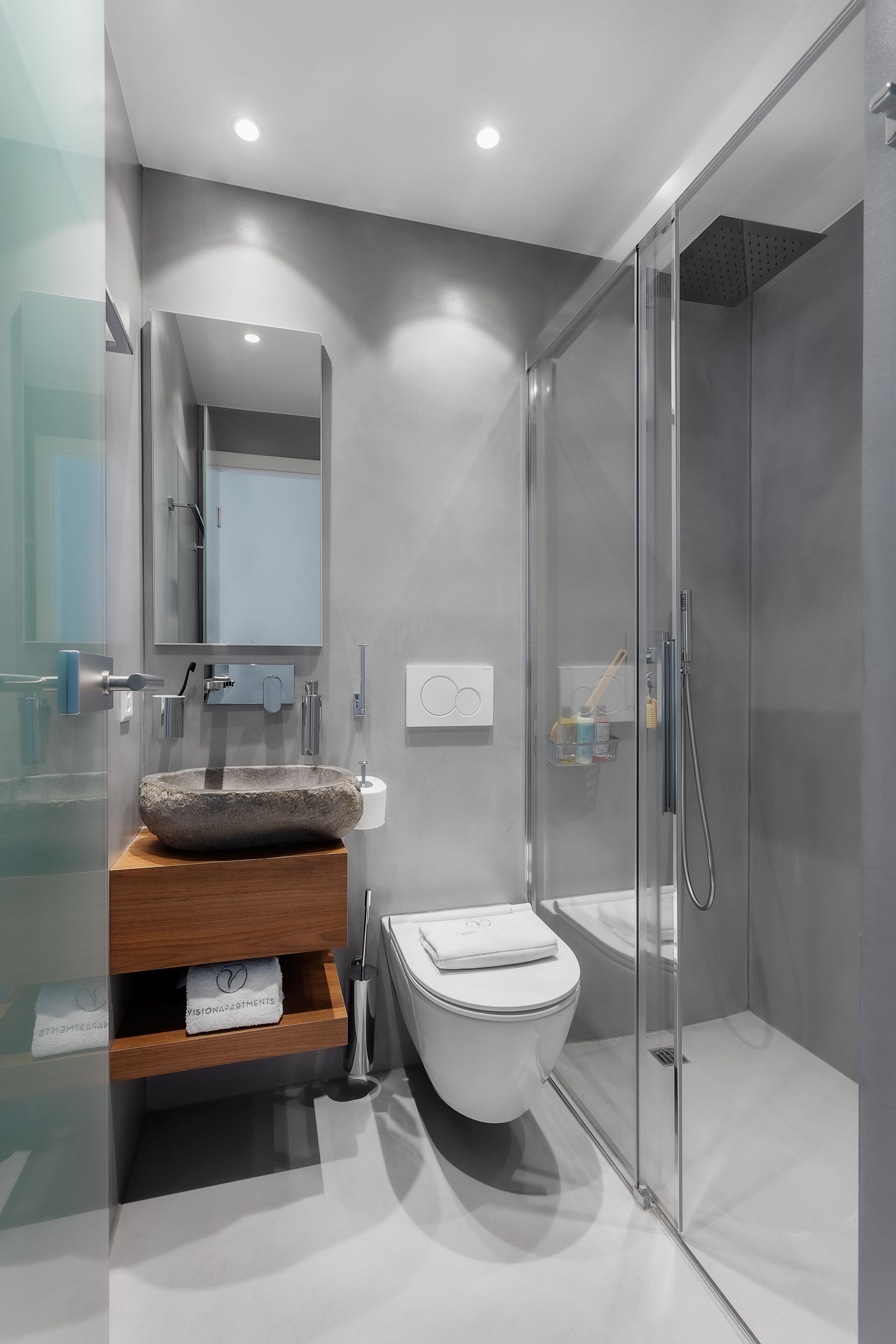 A modern bathroom with a stone sink, a glass shower enclosure, and a white toilet.