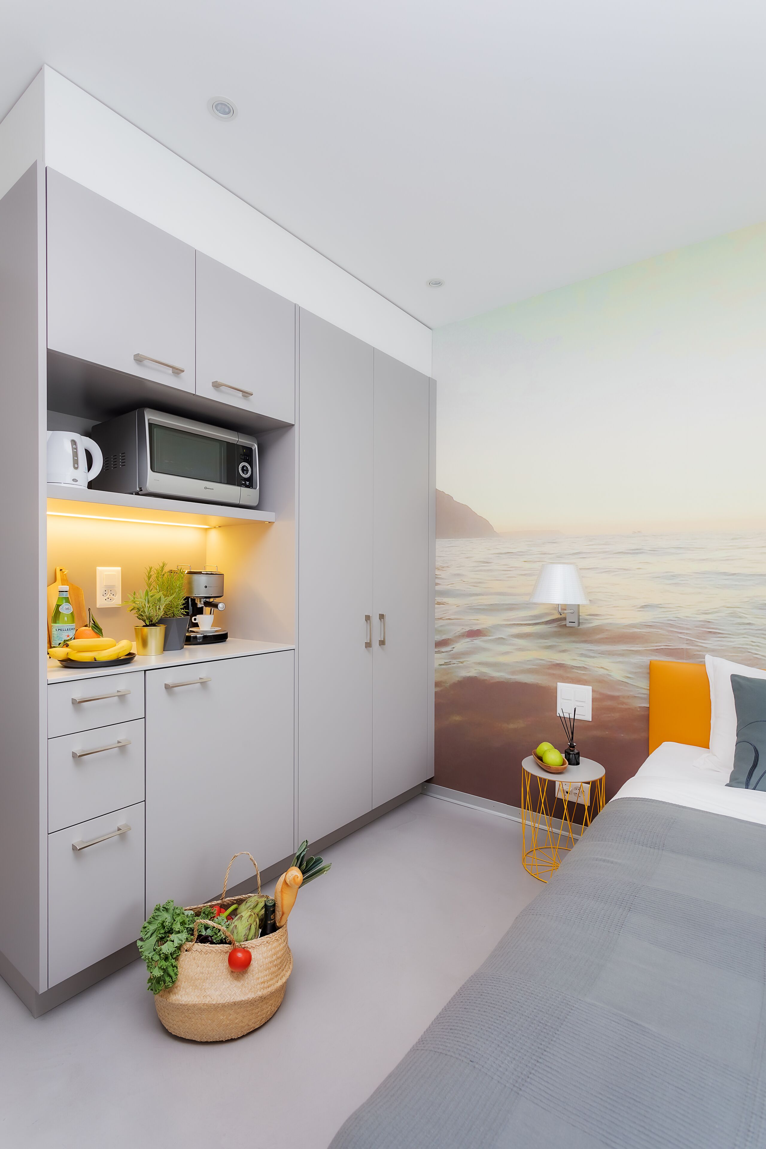 A bedroom with a bed, a nightstand, a wall-mounted lamp, and a view of the ocean.