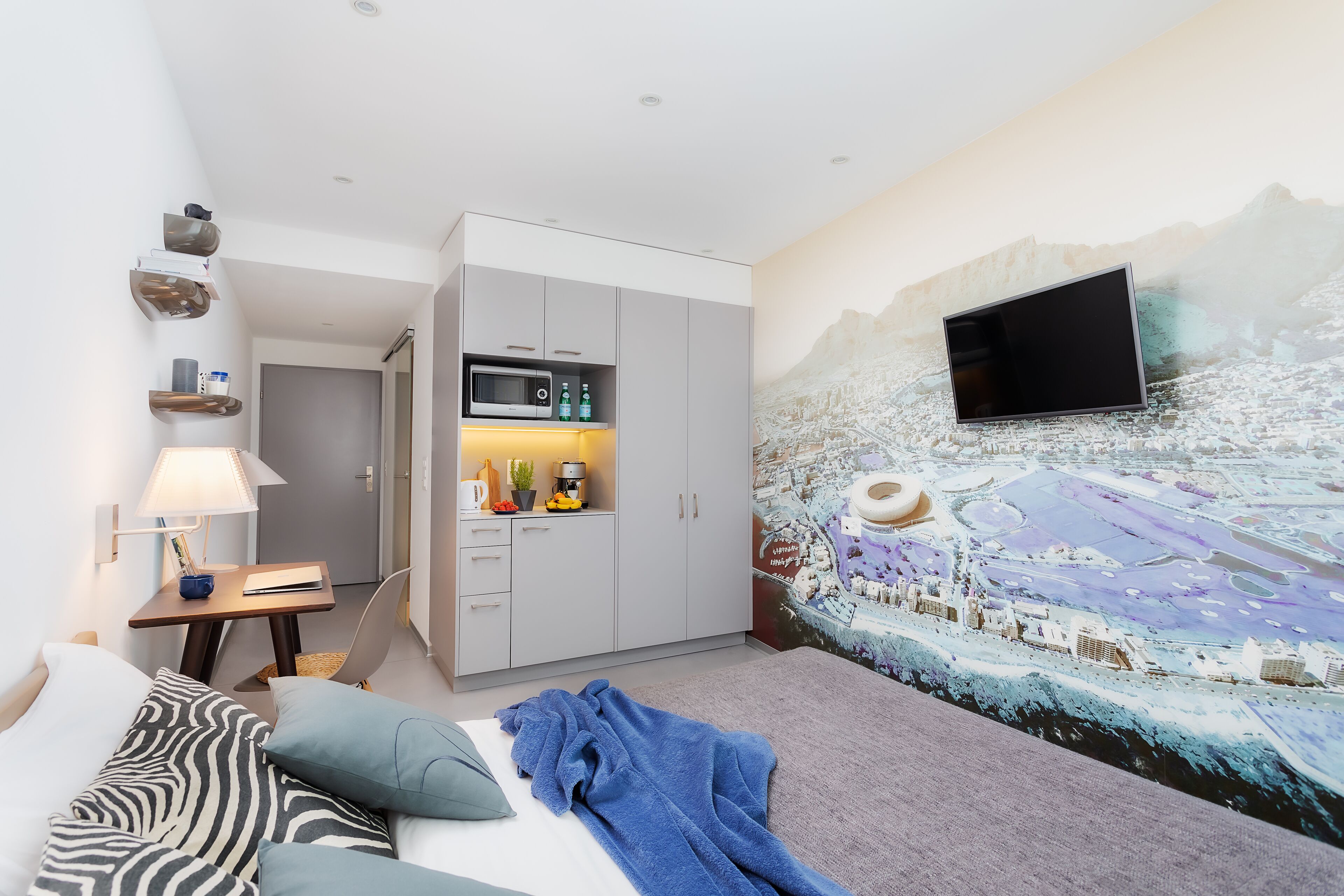 Ein modernes Hotelzimmer mit einem Bett, einem Schreibtisch, einer Mikrowelle und einem an der Wand befestigten Fernseher.