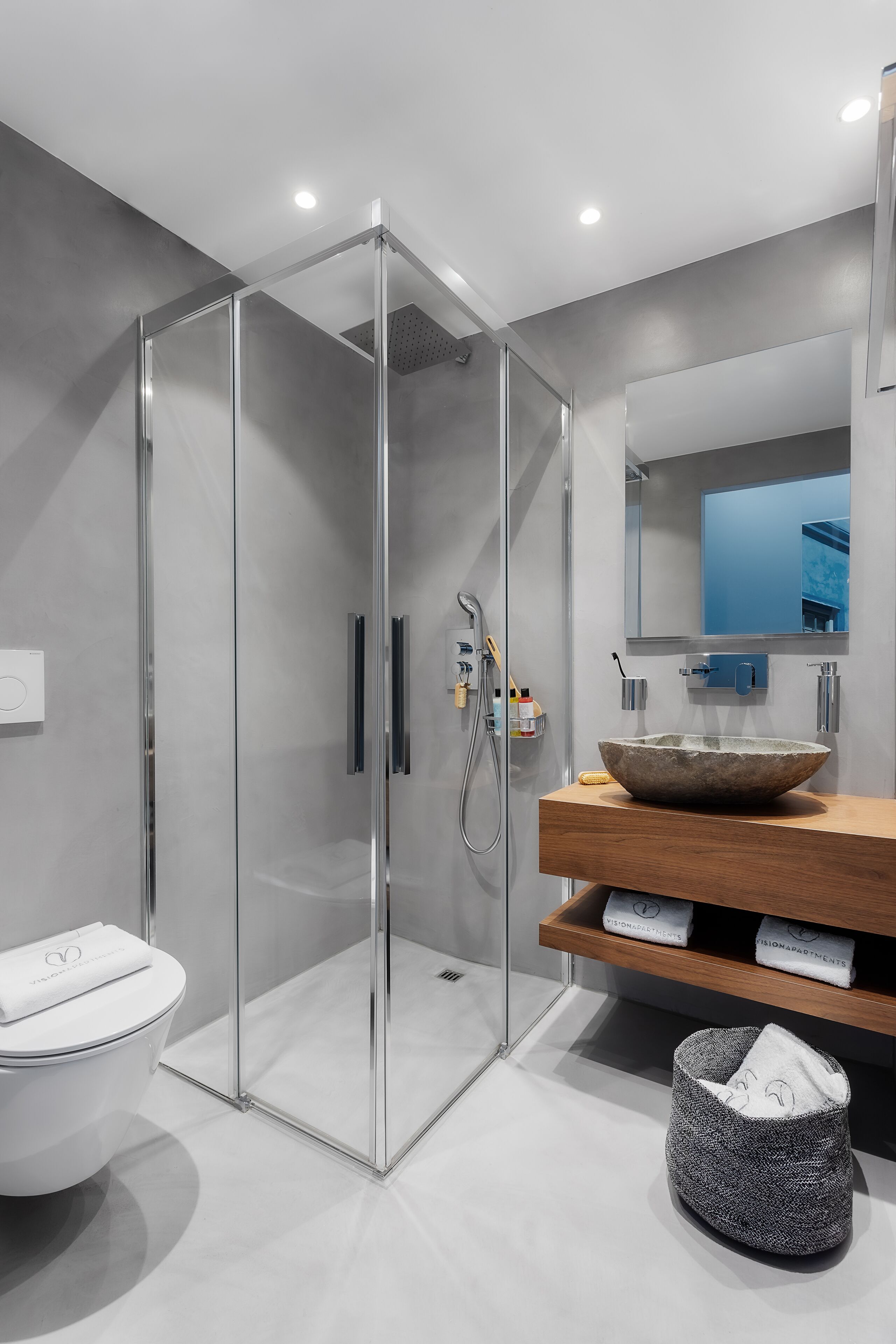 Un baño moderno con ducha de vidrio, tocador de madera con un lavabo grande y un espejo sobre el lavamanos.