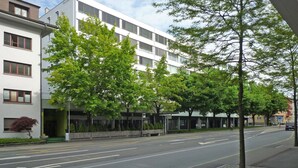 A modern building with multiple floors, large windows, and a green tree in front.