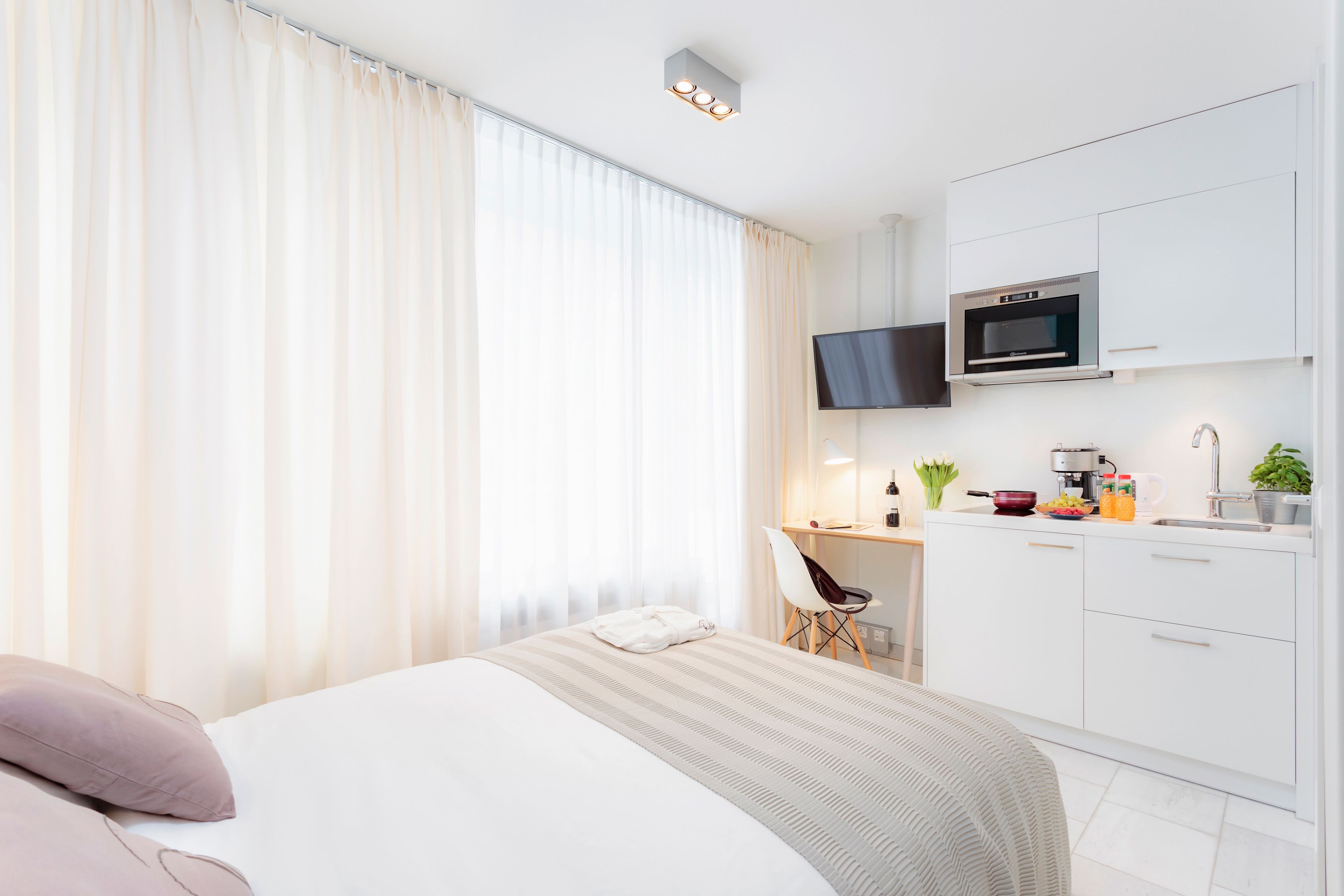 A modern hotel room with a bed, a desk, a flat-screen TV, a microwave, and a small kitchenette.