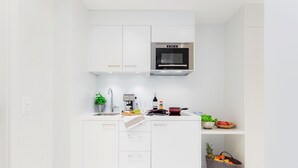 A modern kitchen with white cabinetry, a stainless steel oven, a sink, and a fruit basket.