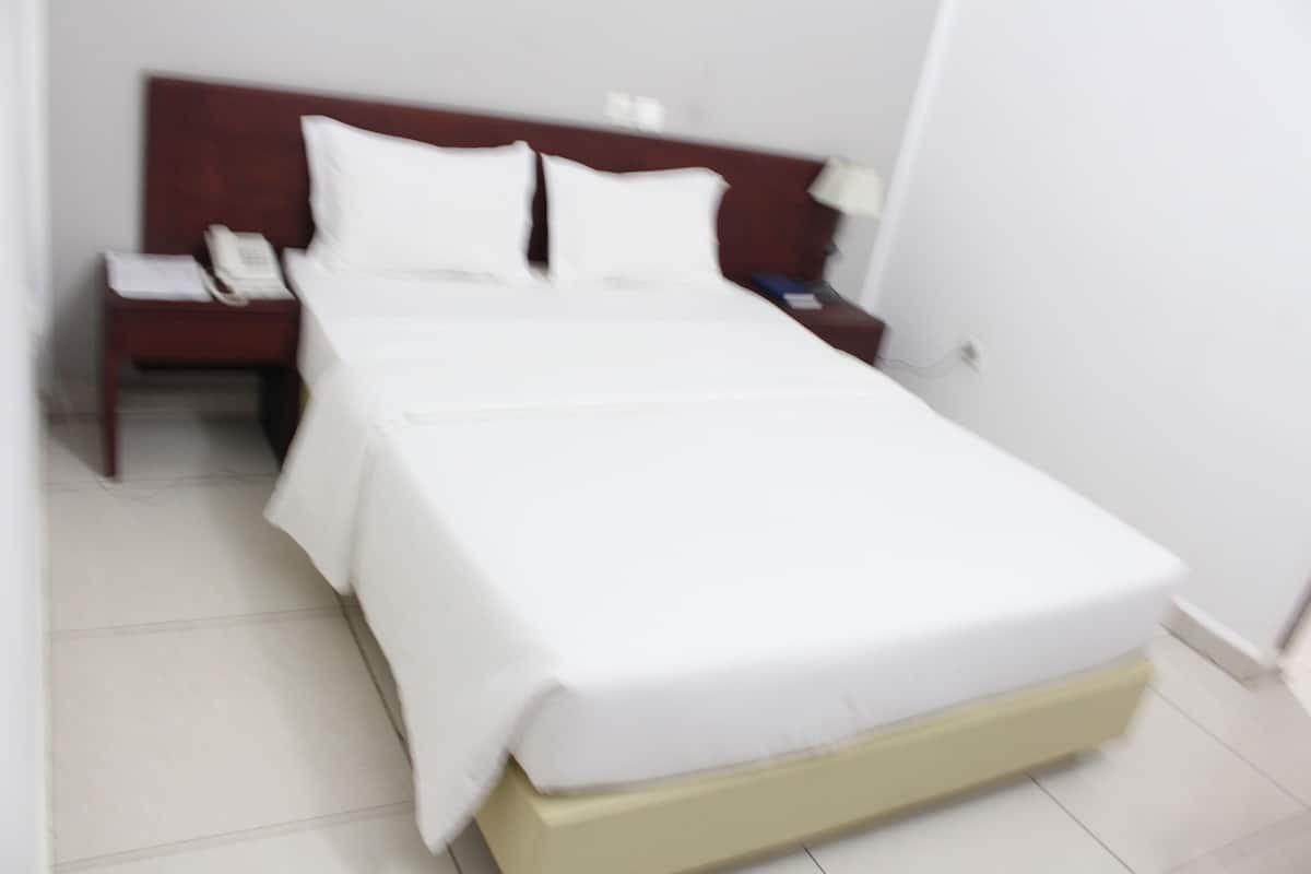 A neatly made bed with white linens, a wooden headboard, and a bedside table with a telephone and papers.