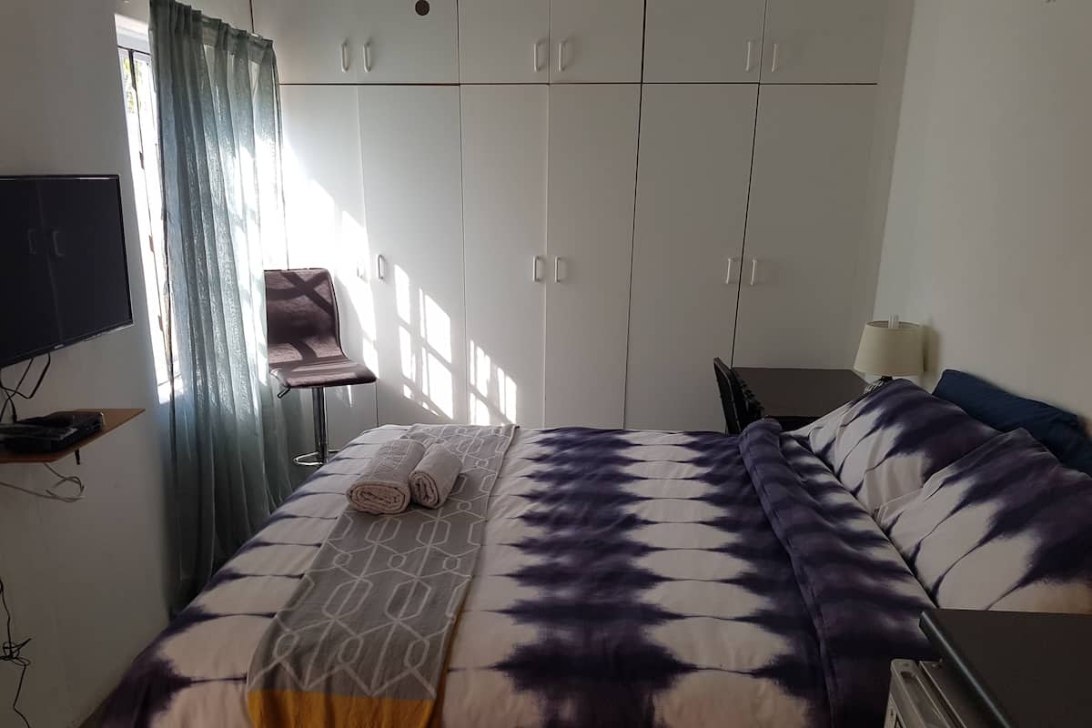 A bedroom with a bed, a TV, a desk, and a wardrobe.