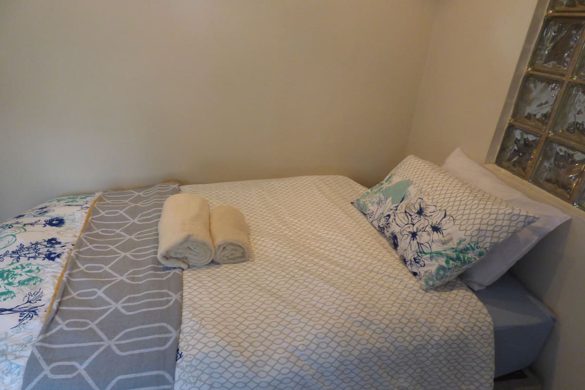 A bed with a patterned bedspread, two rolled towels, and a decorative pillow.