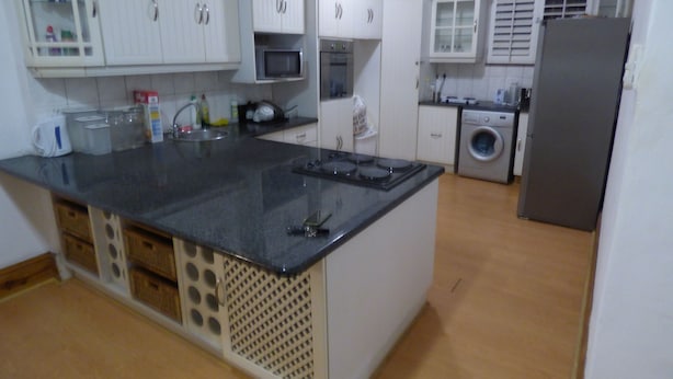 A kitchen with white cabinets, a black countertop, a microwave, a washing machine, and a refrigerator. - Daisy Lodge (Durban)