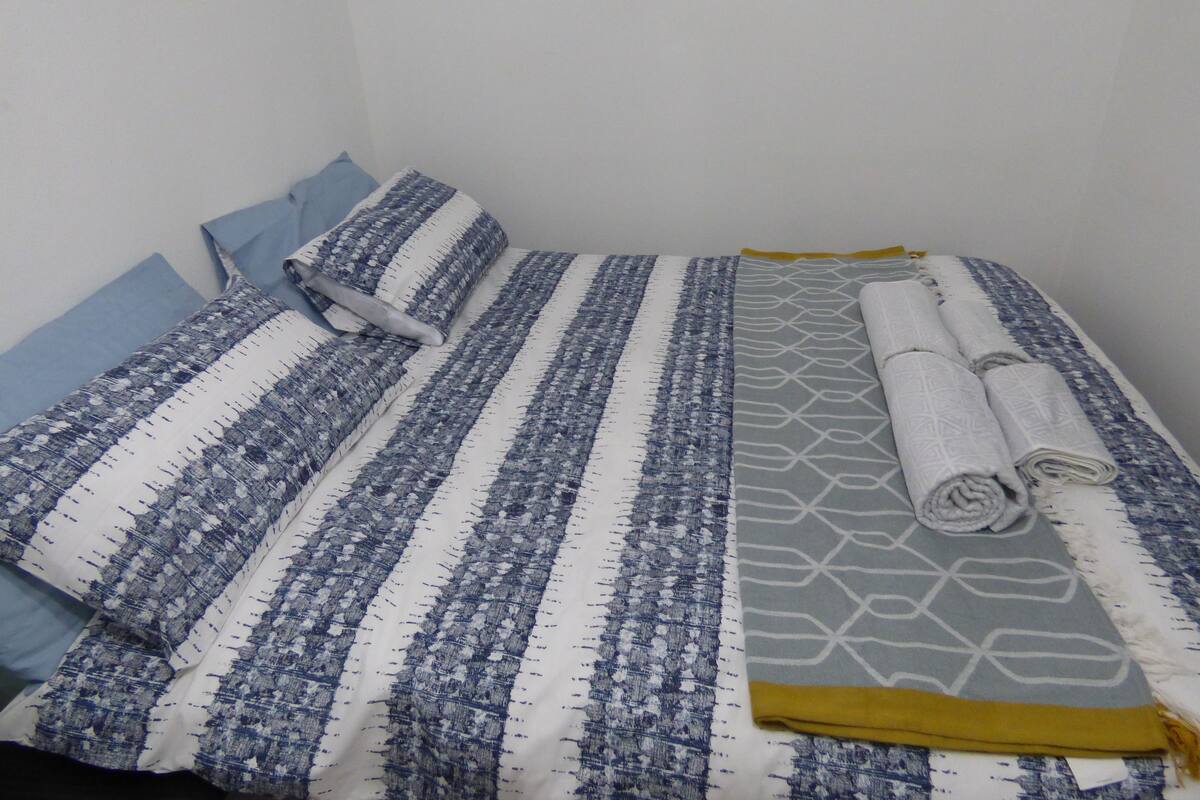A neatly made bed with striped and patterned bedding, a rolled towel, and a folded blanket.
