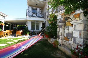 A covered patio with outdoor furniture, a hammock, and a stone wall with a water feature. - Kandira Butik Hotel (Cesme)
