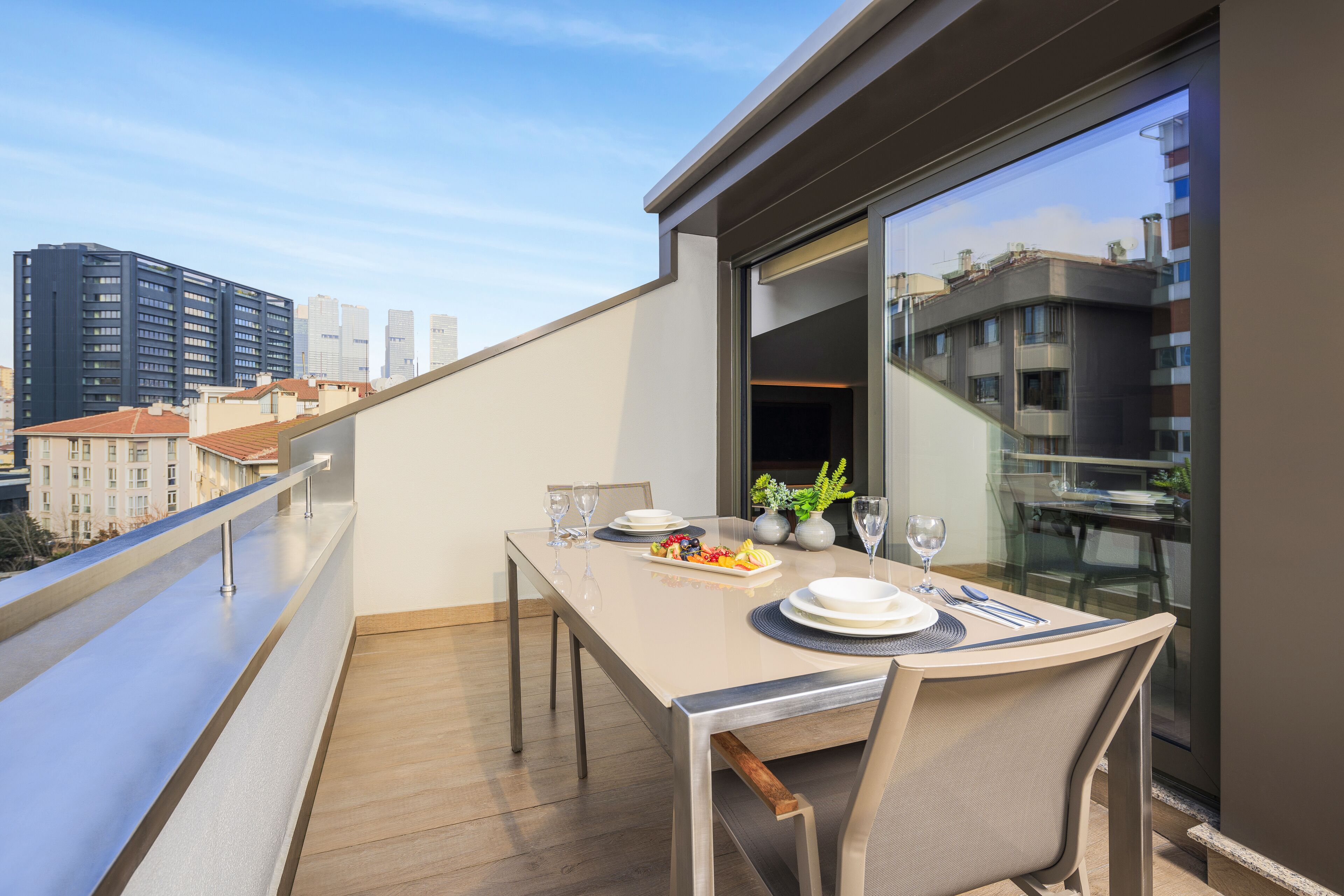 A balcony with a dining table set for two, featuring a city view.