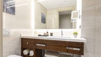 Un bagno moderno con un lavandino bianco, un mobile contenitore in legno e uno specchio sopra. Sul mobile ci sono asciugamani e prodotti per l'igiene personale.