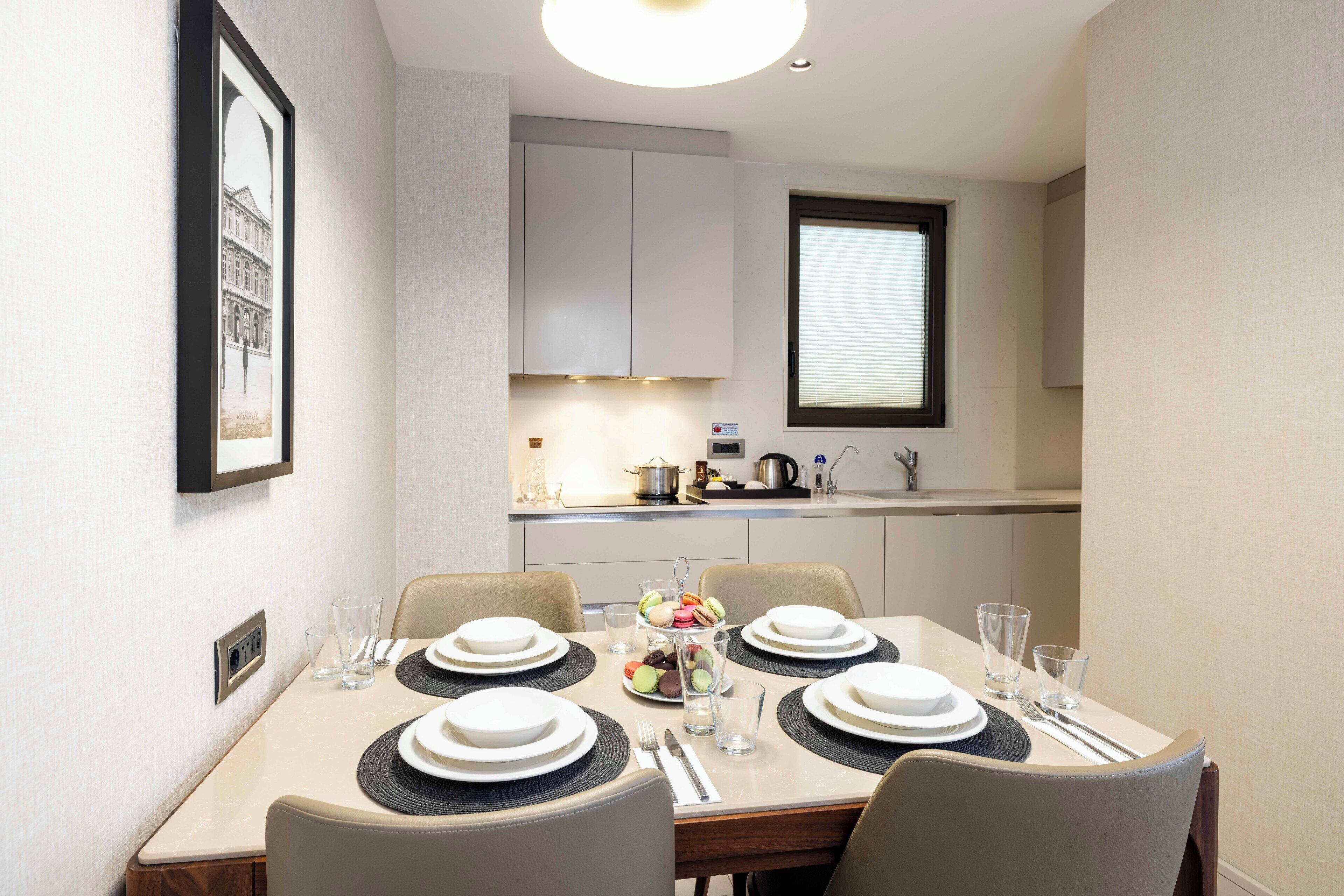 Un coin repas avec une table dressée pour quatre personnes, comprenant des assiettes, des couverts et des verres.