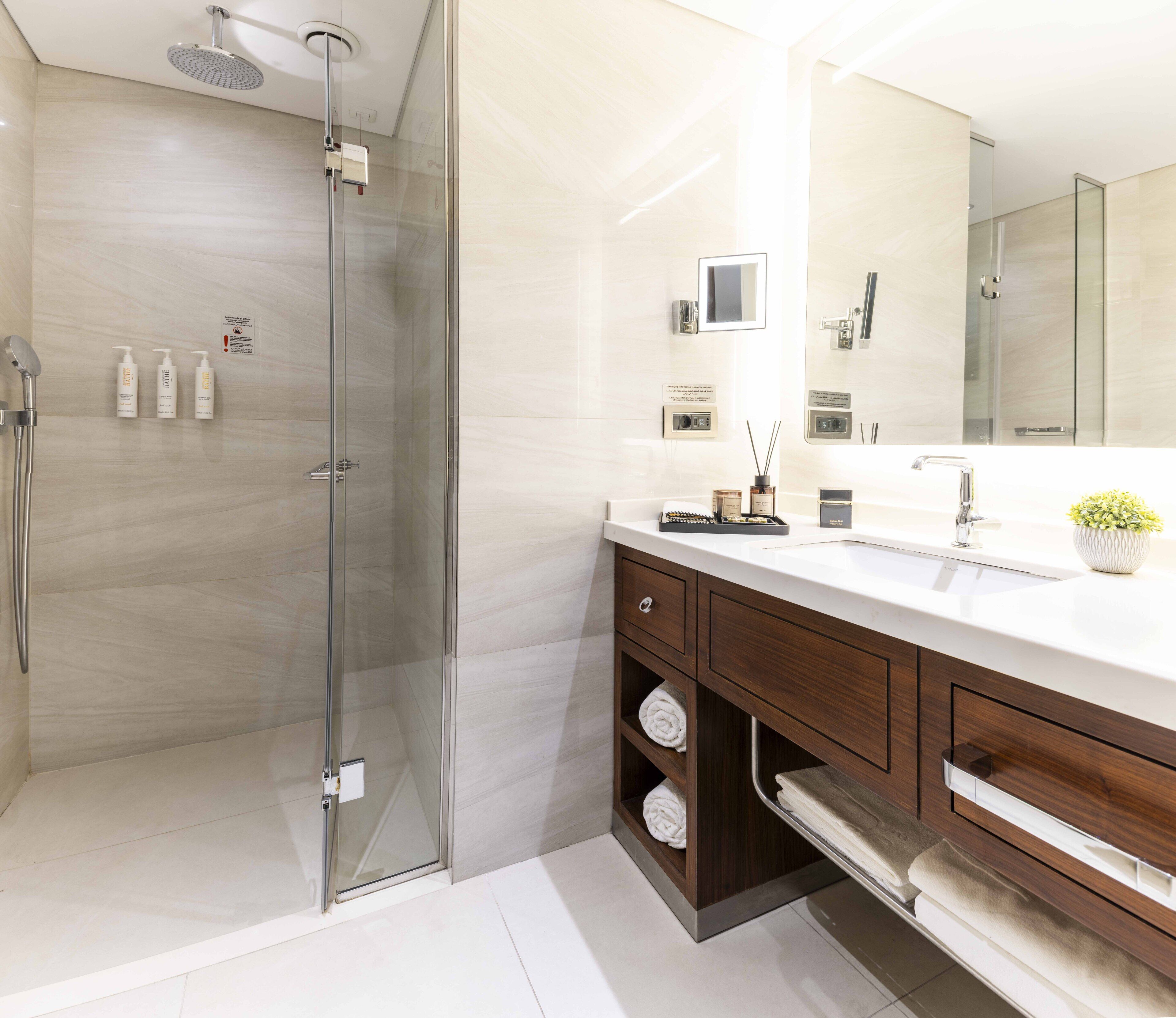 A modern bathroom with a glass-enclosed shower, a white vanity with a mirror, and a wooden cabinet with towels.