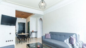 A modern living room with a grey sofa, a glass coffee table, and a dining area with a table and chairs.
